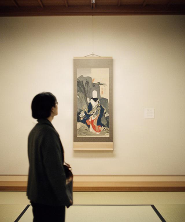 Solo traveller viewing a traditional Japanese artwork in a quiet Kyoto gallery